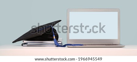 Graduation Cap on notebooks near laptop. Masters or Bachelors Degree thesis writing. Knowledge online courses qualifications and higher education with copy space. Lockdown. Mock up screen