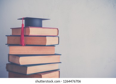 Graduation Cap On Stack Of Many Antique Books On Shelf In Book Store Or Library Room With White Wall Background. Knowledge Learning, Education, Bachelor Degree In University Or Back To School Concept.