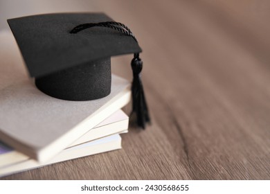 Graduation cap on top of stack of books on a wooden table. Copy space for text. Education concept.