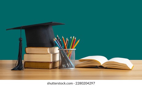 A Graduation cap placed on a stack of books with pencils next to it and an open book on the table. It is the concept of education. - Powered by Shutterstock