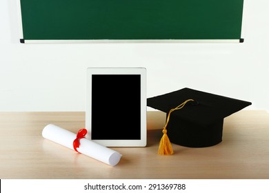 Graduation Cap With Tablet And Diploma On Table In Class