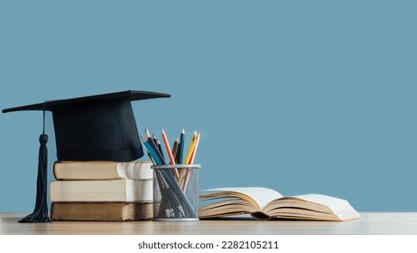 Graduation day.A mortarboard and graduation scroll on stack of books with pencils color in a pencil case on blue background.Education learning concept.