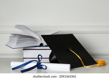 Graduation Hat, Books And Diploma On Floor Near White Wall