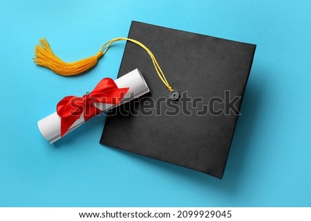 Graduation hat and diploma on light blue background, flat lay