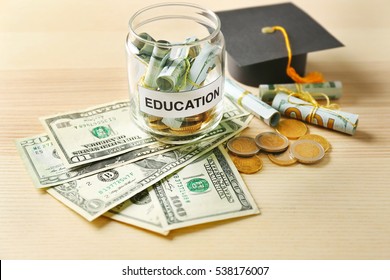 Graduation Hat And Glass Jar With Money For Education On Wooden Table