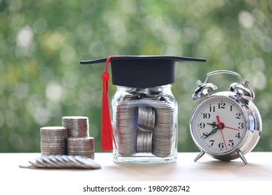 Graduation hat on the glass bottle and alarm clock on natural green background, Saving money for education concept