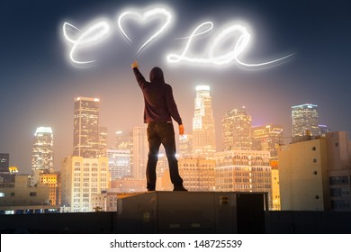 Graffiti artist on rooftop in downtown Los Angeles painting love LA message over night sky with light.