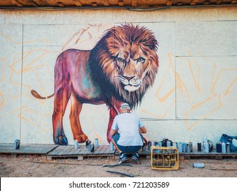 Graffiti Artist Painting On The Street Wall. Man with aerosol spray bottle near the wall. Young talented guy in protective mask drawing colorful lion.