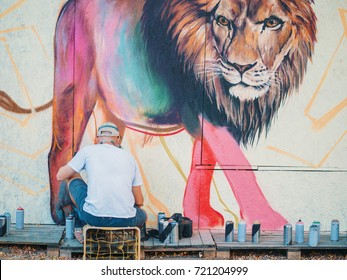 Graffiti Artist Painting On The Street Wall. Man with aerosol spray bottle near the wall. Young talented guy in protective mask drawing colorful lion. - Powered by Shutterstock