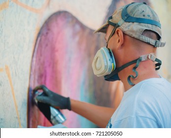 Graffiti Artist Painting On The Street Wall. Man With Aerosol Spray Bottle Near The Wall. Young Talented Guy In Protective Mask Drawing Colorful Lion.