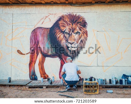 Graffiti Artist Painting On The Street Wall. Man with aerosol spray bottle near the wall. Young talented guy in protective mask drawing colorful lion.