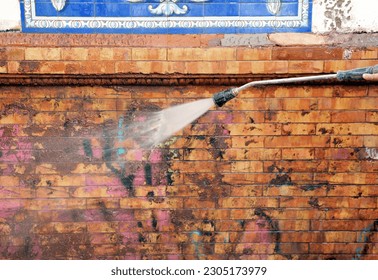 Graffiti cleaning. Worker cleaning a dirty brick and tiles facade with a pressurized water jet in the integral reform of a house. Municipal facade cleaning service - Powered by Shutterstock