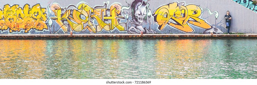 Graffiti writer at the end of his urban paint at river - concept of contemporary artist, lifestyle, street art - Warm filter 