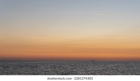 Grain deal cargo delivery, global food crisis. Ship in the distance on the horizon after sunset. Inversion white traces in the sky from flying planes. Сlear sky over a calm sea.  - Powered by Shutterstock