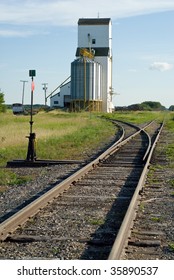 A grain elevator situated near a set of railroad tracks with the rails ending in a vanishing point