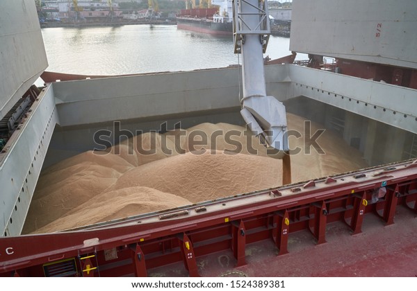 Grain loading in hold of bulk carrier ship\
with elevator crane closeup. Port grain elevator. Industrial sea\
trading port bulk cargo zone grain\
terminal