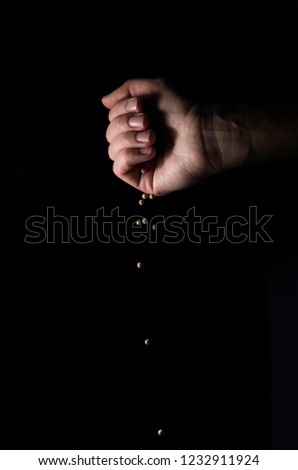 Grains of yellow pepper in a woman's fist falling down on black background