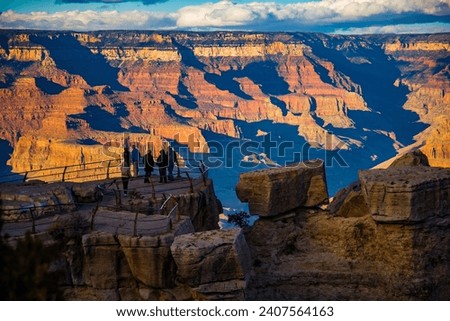 Grand Canyon National Park, Arizona.  A group of tourists gather at a viewpoint on the south rim as the sun is casting long shadows