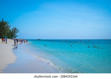 Grand Cayman, Cayman Islands, June 2021 People On Seven Mile Beach Watching Swimmers In The Caribbean Sea During A Competition