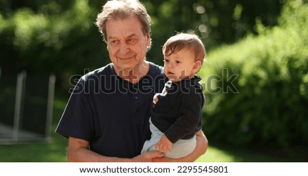Grand father bonding with toddler outdoors. Grand-parent holding grand-child in arms