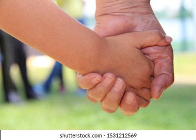 Grand Father Is Holding Small Child By Hands
