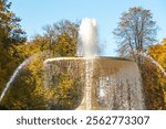 A grand fountain spraying water gracefully, surrounded by vibrant autumn foliage under a clear blue sky.