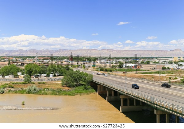 GRAND JUNCTION, USA - MAY 28,\
2016: Highway bridge over the confluence of the Gunnison River and\
Colorado River with part of the city and the Book Cliffs in the\
back.