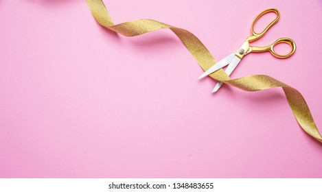 Grand Opening Concept. Gold Scissors Cutting Golden Ribbon Against Pink Background, Copy Space, Top View.