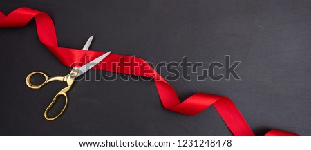 Grand opening invitation card template. Gold scissors cutting red silk ribbon against black background, Top view, banner, copy space.