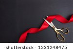 Grand opening. Top view of gold scissors cutting red silk ribbon against black background, copy space