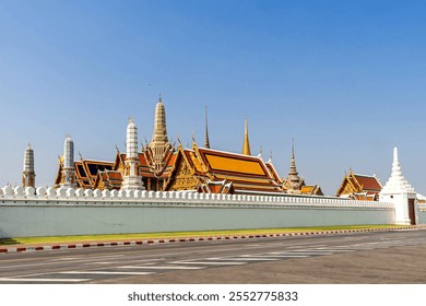 The Grand Palace in Bangkok, Thailand, iconic architectural landmark with golden spires and traditional Thai design under a clear blue sky, viewed from the street - Powered by Shutterstock