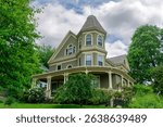 Grand Queen Anne Victorian house with turret among green summer trees in Newton, Massachusetts, USA
