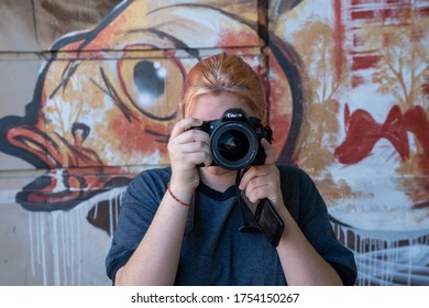 Grand Rapids, MI, USA - June 08, 2020 - Teen Girl Using A Cannon 60D With A Mural In The Background Holding A Phone With A Snapchat App Notification. High Quality Photo