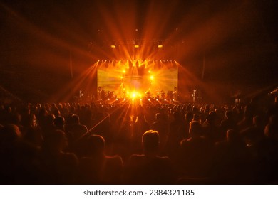 A grand show with vibrant orange lights, a crowd of fans eagerly gazing at the stage, brilliant and beautiful lights resembling sun rays. A rock concert or a pop concert atmosphere. - Powered by Shutterstock