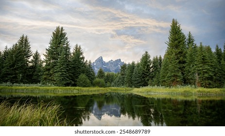 Grand Tetons reflected in river in Grand Teton National Park. Snow capped mountains in Wyoming reflected in pond. Green trees framing jagged mountains with cloudy sky. - Powered by Shutterstock