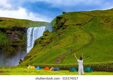 Grand Waterfall Skogafoss. Near A Waterfall Put Some Colorful Tourist Tents. Elderly Woman Shocked By The Beauty Of The Waterfall