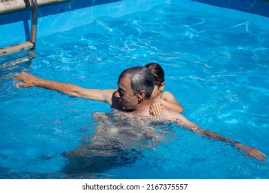 Grandad And Grandson Playing In The Swimming Pool In The School Summer Holidays While The Parents Are Working