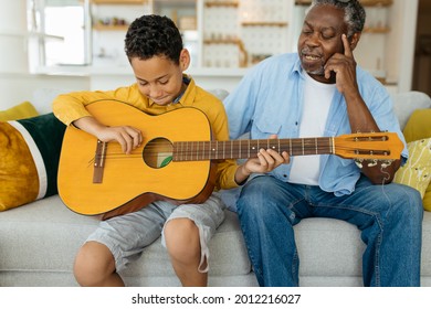 Grandchild sitting with his grandpa in the living room and playing the guitar. Experienced old man listening to a youngster. - Powered by Shutterstock