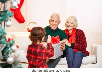 Grandchild Taking Photo Of Grandparents With Smartphone At Christmas