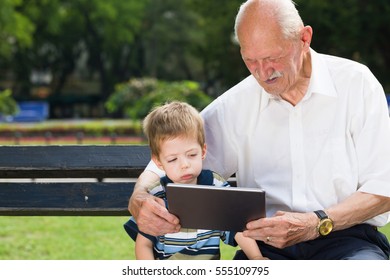 Grandchild teaching to his grandfather to use tablet on a bench