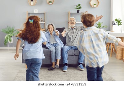 Grandchildren boy and girl running to their senior happy smiling grandparent sitting on sofa at home to hug. Kids enjoying leisure time with grandma and grandpa. Family leisure concept. - Powered by Shutterstock