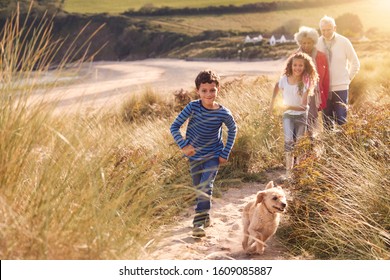 Grandchildren And Pet Dog Exploring Sand Dunes With Grandparents On Winter Beach Vacation