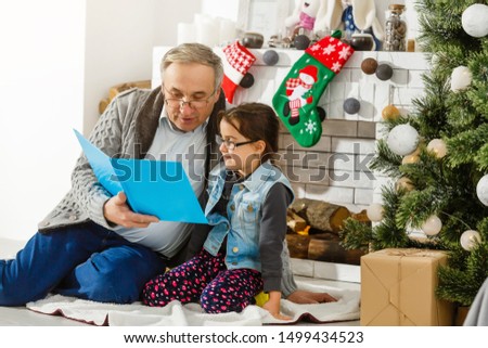 granddaughter and grandfather are sitting near the fireplace and reading