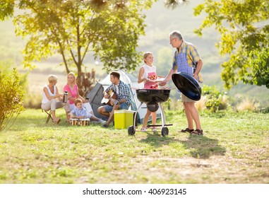 Granddaughter Helping  Grandfather Grilling For Family
