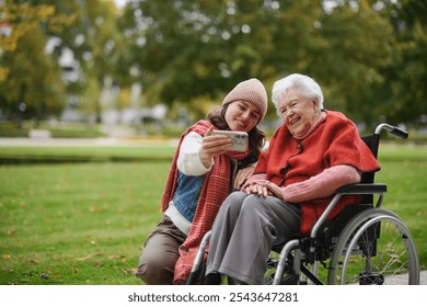 Granddaughter on an autumn walk in the park with her grandmother in wheelchair, taking selfie with smartphone. - Powered by Shutterstock