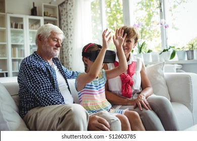 Granddaughter using virtual reality headset with her grandparents in living room at home - Powered by Shutterstock