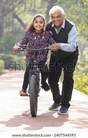 Grandfather assisting playful granddaughter in riding bicycle at park