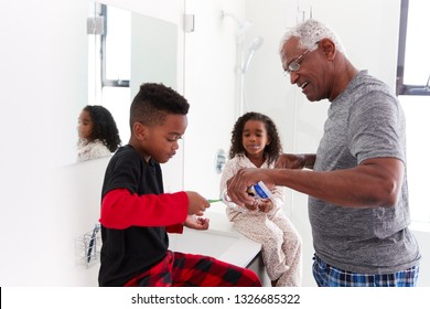 Grandfather In Bathroom Wearing Pajamas Helping Grandchildren To Brush Teeth - Powered by Shutterstock