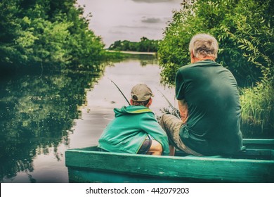 Grandfather And Boy Fishing Together. HDR. Boy And An Old Man Sitting In A Boat With A Fishing Rod. View From The Back