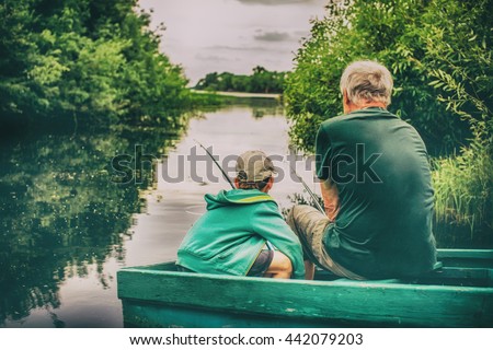 grandfather and boy fishing together. HDR. boy and an old man sitting in a boat with a fishing rod. view from the back